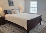 Thumbnail 4 of 9 - A bed with a white sheet and a white pillow is in the middle of a room with a window.