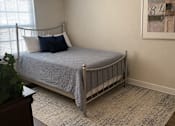 Thumbnail 5 of 9 - A bedroom with a bed, a rug, and a painting on the wall.