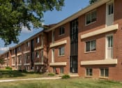 Thumbnail 1 of 19 - A long brick building with a green lawn in front at Winston Apartments, Baltimore, Maryland
