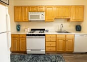 Thumbnail 5 of 23 - Kitchen with white appliances and wooden cabinets at Rockdale Gardens Apartments*, Baltimore.