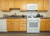 Thumbnail 1 of 20 - A kitchen with wooden cabinets and a white stove top oven. at Colony Hill Apartments & Townhomes, Baltimore, MD