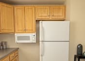 Thumbnail 6 of 26 - A white refrigerator in a kitchen with wooden cabinets.