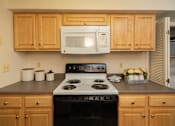 Thumbnail 11 of 36 - A kitchen with a white microwave above a stove and wooden cabinets.at Chapel Valley Townhomes, Maryland, 21236