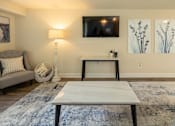 Thumbnail 4 of 27 - A living room with a grey couch, a white coffee table, a lamp, a TV, and two paintings on the wall.at Deer Park Apartments, Randallstown, MD