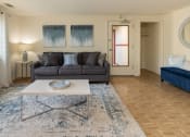 Thumbnail 3 of 19 - A living room with a grey couch, a white coffee table, and a blue rug at Winston Apartments, Baltimore, Maryland