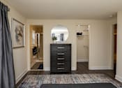 Thumbnail 14 of 32 - A black dresser with a round mirror above it in a room with a grey carpet. Spring Hill Apartments & Townhomes, Baltimore, MD 21234