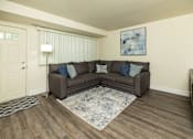 Thumbnail 3 of 22 - A brown couch with blue pillows sits in a room with wooden floors and a white door.