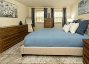 Thumbnail 14 of 22 - A bedroom with a blue bedspread and a wooden headboard.