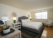 Thumbnail 6 of 10 - A bedroom with a bed, chair, and a flower vase on a table.