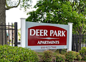 Thumbnail 11 of 11 - A sign for Deer Park Apartments is displayed in front of a fence and greenery.