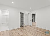 Thumbnail 20 of 23 - A spacious room with white walls and wooden flooring, featuring a walk-in closet with shelves and a mirror.