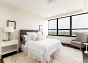 Thumbnail 2 of 33 - A bedroom with a large bed, a nightstand with a lamp, a chair, and a window with a view.