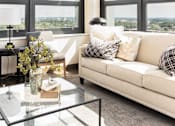 Thumbnail 16 of 33 - A modern living room with a glass coffee table and a large window.