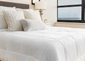 Thumbnail 11 of 33 - A bed with white bedding and a white pillow is in front of a window.