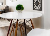 Thumbnail 28 of 33 - A white table with a green plant on it and a white chair in front of it.