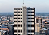 Thumbnail 21 of 33 - A tall building with a flag on top stands in the middle of a cityscape.