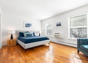 Thumbnail 5 of 21 - A bedroom with hardwood-style flooring, two large windows, and a portable cooling/heating unit on the wall.