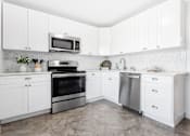 Thumbnail 4 of 21 - A bright and spacious kitchen with white cabinets, herringbone tile backsplash, stainless steel appliances, and tile-style flooring.