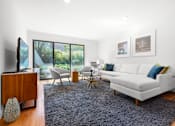 Thumbnail 3 of 21 - A modern living room with recessed lighting, hardwood-style flooring, and three large sliding doors to a private patio with lush greenery.