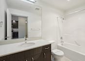 Thumbnail 15 of 43 - A white sink with a mirror above it and a toilet next to a bathtub.