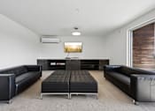 Thumbnail 38 of 43 - A black leather couch and ottoman are in a white room with a television.