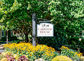 Thumbnail 2 of 24 - A sign for Carriage House Apartments is surrounded by flowers.