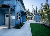 Thumbnail 20 of 55 - A blue building with a white door and windows is surrounded by greenery.