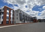 Thumbnail 8 of 16 - A row of modern buildings with a cloudy sky in the background.