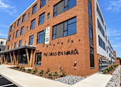 Thumbnail 1 of 16 - The Oaks on Maria is a brick building with a parking lot in front.