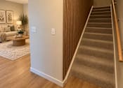Thumbnail 14 of 16 - A staircase with a wooden handrail and carpeted steps leads to an upper level.
