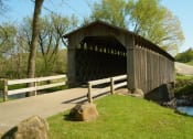 Thumbnail 13 of 22 - a covered bridge is next to a road and a river at The Daniels at Northern Gateway Apartments, Saukville, WI 53080