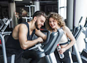 Thumbnail 3 of 16 - A man and a woman are working out on exercise machines in a gym.