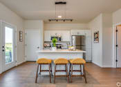 Thumbnail 18 of 22 - A kitchen with white cabinets and a white island with three stools in front.