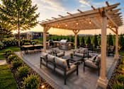 Thumbnail 4 of 30 - A wooden pergola with string lights is over a patio with grey couches and a table.