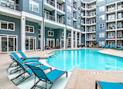 Thumbnail 23 of 26 - a swimming pool with blue chairs in front of an apartment building