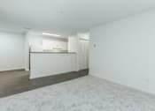 Thumbnail 19 of 37 - A white room with a carpeted floor and a kitchen area in the background.