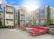 Thumbnail 22 of 30 - A sunny day at a modern apartment complex with a red seating area.
