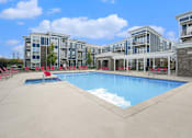 Thumbnail 1 of 30 - A large swimming pool in front of a building with red lounge chairs.