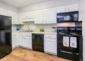 Thumbnail 1 of 41 - Chattanooga, TN, Pet-Friendly Apartments - Riverview North - Kitchen with Wood-Style Flooring, Efficient Black Appliances, White Cabinetry, Cream Tile Backsplash, and Cream Countertops.