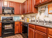 Thumbnail 11 of 34 - A kitchen with brown cabinets and black appliances.