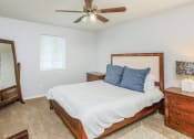 Thumbnail 6 of 41 - Dog-Friendly Apartments in Chattanooga, TN - Riverview North - Bedroom with Carpeted Flooring, Large Bed, Nightstands with Drawers, Dresser, Framed Mirror, Ceiling Fan, White Walls, and Window with Blinds.