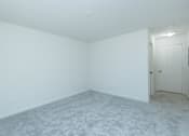 Thumbnail 21 of 37 - A white room with a carpeted floor and a door on the right side.