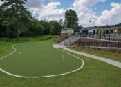 Thumbnail 35 of 46 - a synthetic turf putting green with a clubhouse and pavilion in the background