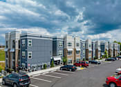 Thumbnail 30 of 31 - A row of modern apartment buildings with cars parked in the lot.