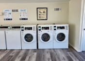 Thumbnail 30 of 31 - A row of white front load washing machines are lined up in a laundry room.
