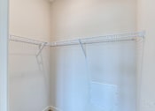 Thumbnail 38 of 40 - a walk in closet with a white wall and a wire shelf on top of it