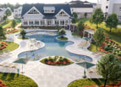 Thumbnail 1 of 43 - Luxury Apartments for Rent in Madison, AL - Paxton Place - Lazy River-Style Swimming Pool with Cabanas, Sundeck, Lounge Seats, Tables and Chairs, and Surrounding Manicured Plants and Trees.