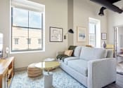 Thumbnail 4 of 25 - A living room with a grey couch, a round glass table, and a ceiling fan.