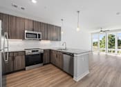 Thumbnail 24 of 34 - Upscale Apartments in Huntsville, AL - The Arcadia - Kitchen with Luxury Vinyl Plank Flooring, Peninsula, Pendant Lights, Granite Countertops, Stainless-Steel Appliances, and View of Living Area.