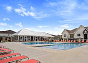 Thumbnail 22 of 36 - A swimming pool surrounded by red sun loungers and a building in the background.